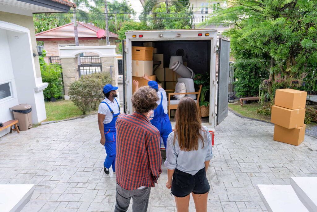 A couple standing with their backs to the camera looking at movers and a moving truck