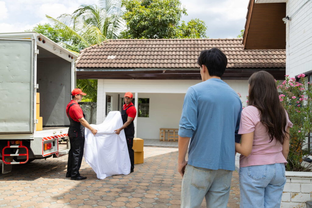 A couple standing with their backs to the camera while movers are carrying furniture in the background